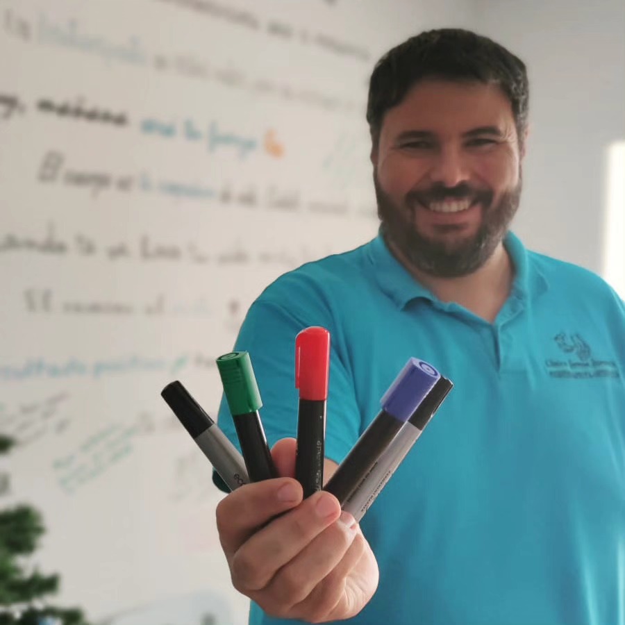 Alejandro sosteniendo cuatro rotuladores ante la pared llena de mensajes