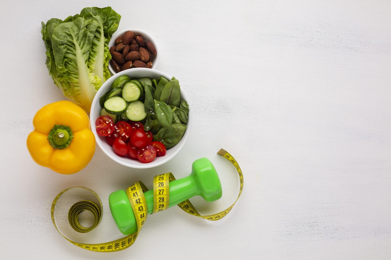 Bol de ensalada junto a unas pesas, alimentación saludable y ejercicio